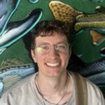 Zach in front of a colorful background with images of fish and other sea life.