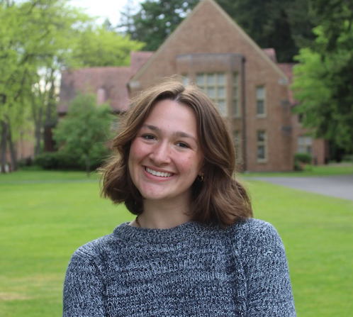 Jordan standing outside in front of a building, wearing a blue sweater.