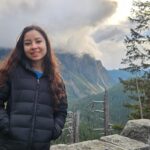 Gaby in a coat standing outside near a mountain.