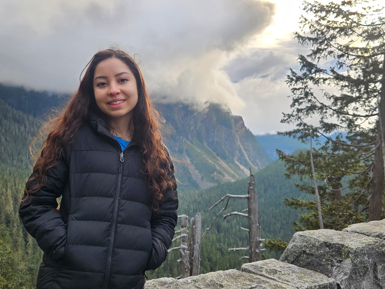 Gaby in a coat standing outside near a mountain.