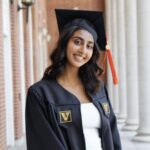 Riya standing in front of white columns in her commencement cap and gown.