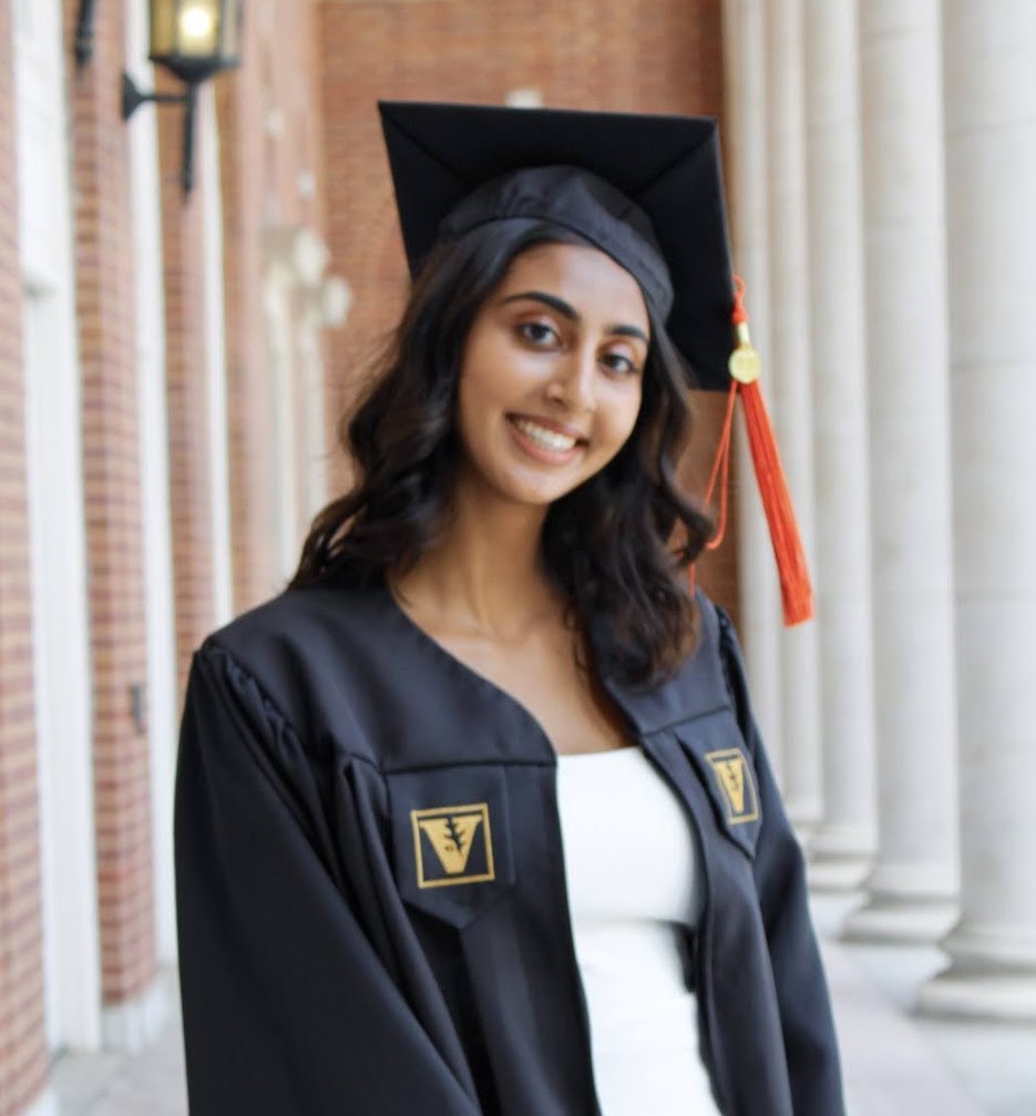 Riya standing in front of white columns in her commencement cap and gown.